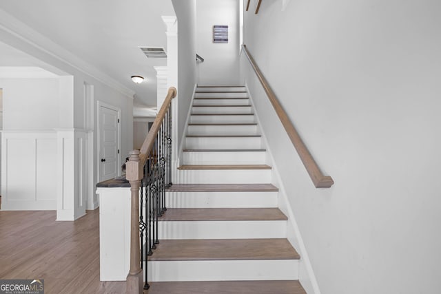 staircase with a wainscoted wall, visible vents, a decorative wall, ornamental molding, and wood finished floors