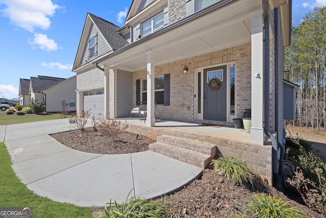 view of exterior entry with a porch, concrete driveway, and brick siding