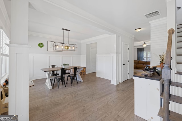 dining room with light wood-style flooring, ceiling fan with notable chandelier, visible vents, stairs, and crown molding