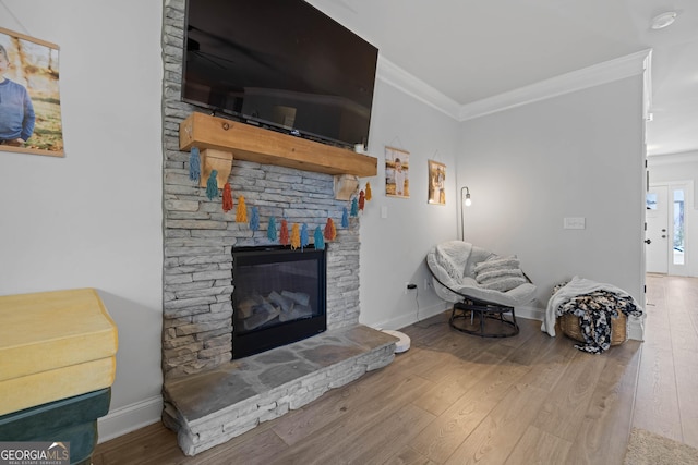 living room with crown molding, baseboards, wood finished floors, and a stone fireplace