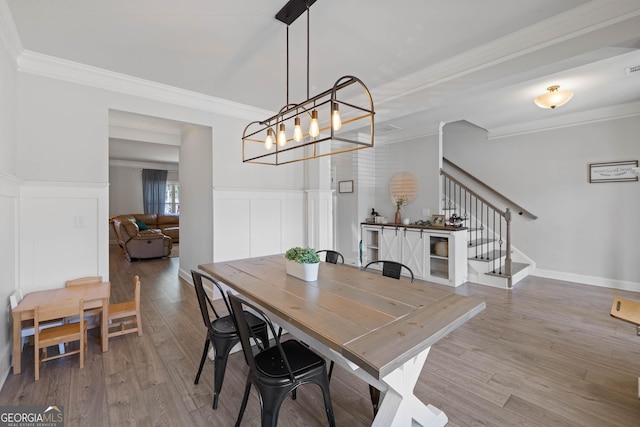 dining room featuring a wainscoted wall, stairway, wood finished floors, and ornamental molding