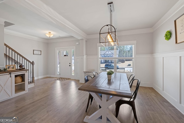 dining area with stairs, a decorative wall, crown molding, and light wood-style floors