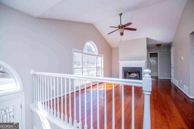 unfurnished living room with baseboards, a fireplace with raised hearth, ceiling fan, dark wood-style flooring, and vaulted ceiling