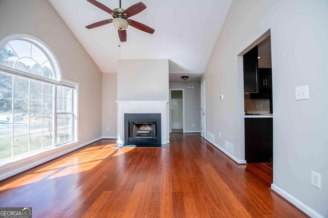 unfurnished living room featuring a fireplace with flush hearth, wood finished floors, visible vents, and baseboards