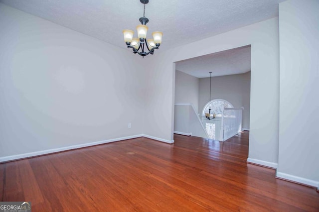 empty room featuring dark wood finished floors, a textured ceiling, and an inviting chandelier