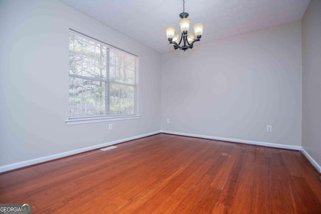 spare room featuring a chandelier, visible vents, baseboards, and wood finished floors