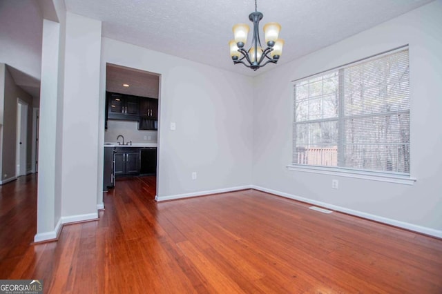 unfurnished dining area with dark wood-style flooring, a sink, a textured ceiling, a chandelier, and baseboards