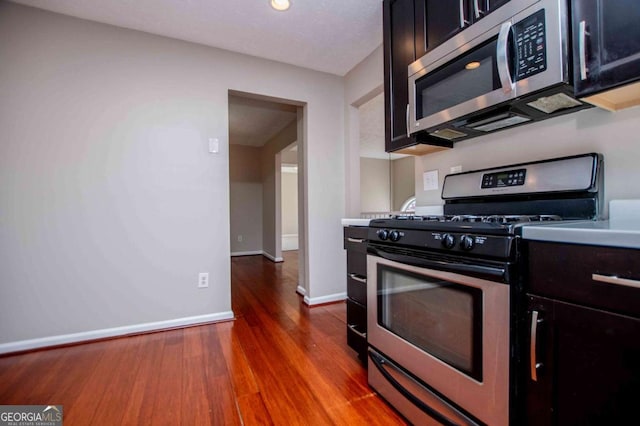 kitchen with appliances with stainless steel finishes, light countertops, dark wood finished floors, and baseboards