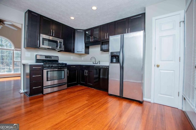 kitchen with glass insert cabinets, appliances with stainless steel finishes, light countertops, light wood-type flooring, and a sink