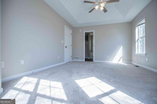 spare room with a raised ceiling, visible vents, a ceiling fan, light carpet, and baseboards