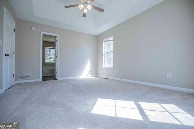 carpeted empty room with a tray ceiling, a ceiling fan, visible vents, and baseboards