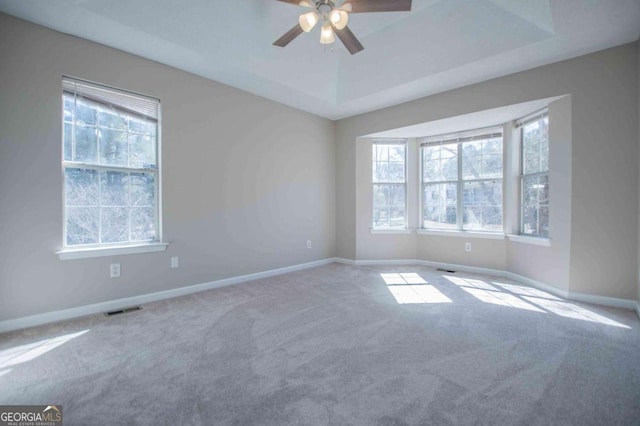 spare room with a tray ceiling, visible vents, light carpet, and baseboards