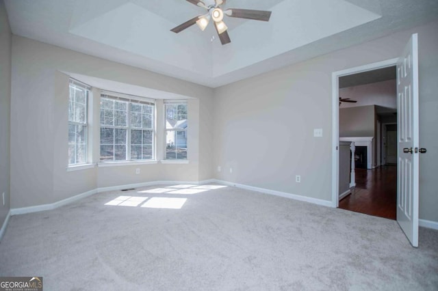 empty room featuring a ceiling fan, a raised ceiling, dark carpet, and baseboards