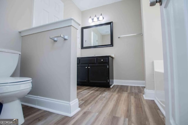 full bathroom featuring toilet, baseboards, wood finished floors, and vanity