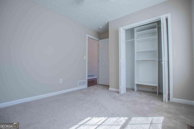 unfurnished bedroom with a textured ceiling, light carpet, visible vents, baseboards, and a closet