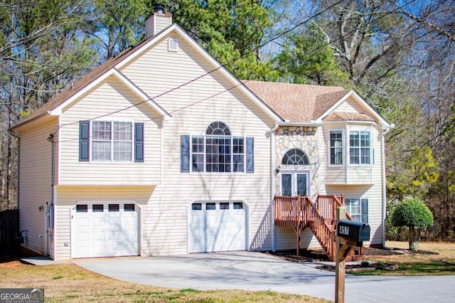 raised ranch with driveway, stone siding, a chimney, roof with shingles, and an attached garage