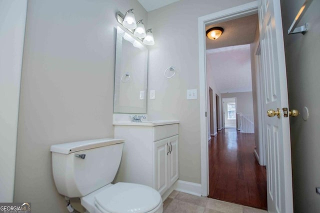 half bath with tile patterned flooring, baseboards, vanity, and toilet