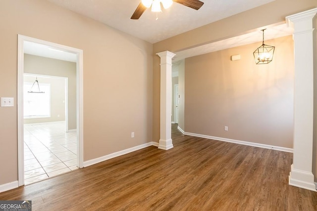 empty room with a ceiling fan, decorative columns, baseboards, and wood finished floors