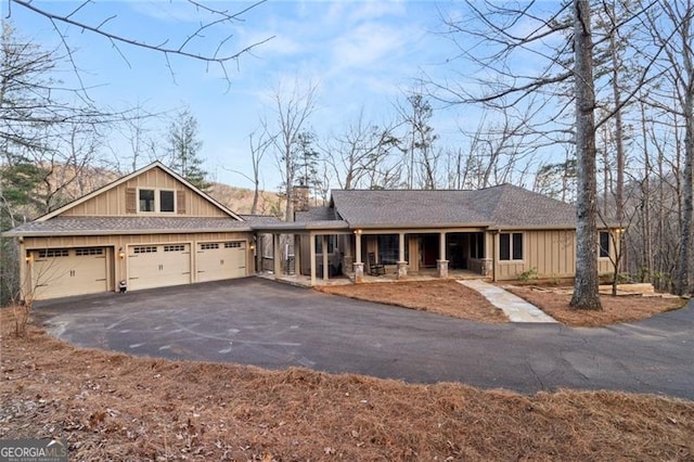 view of front of house with driveway, a chimney, an attached garage, covered porch, and board and batten siding