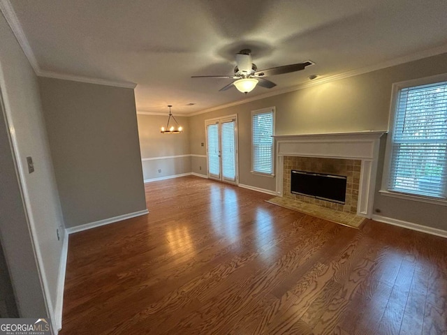 unfurnished living room featuring ornamental molding, dark wood finished floors, a tiled fireplace, and ceiling fan with notable chandelier