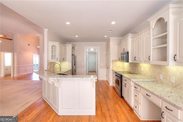 kitchen featuring appliances with stainless steel finishes, glass insert cabinets, white cabinets, a sink, and light stone countertops