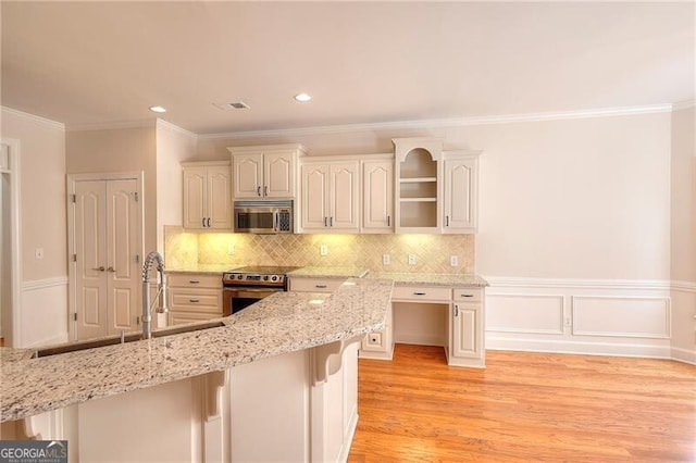 kitchen featuring tasteful backsplash, light wood-style flooring, appliances with stainless steel finishes, wainscoting, and light stone countertops