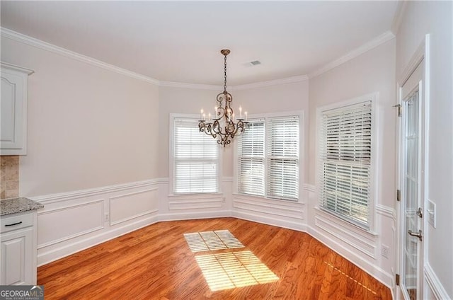 unfurnished dining area featuring a chandelier, ornamental molding, wainscoting, and light wood-style floors