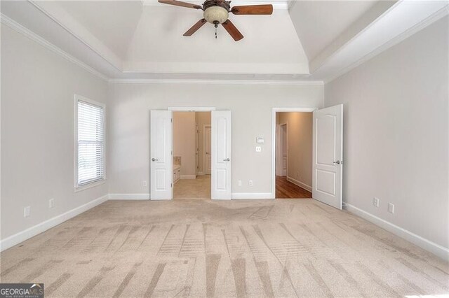 unfurnished bedroom with baseboards, a tray ceiling, crown molding, and light colored carpet