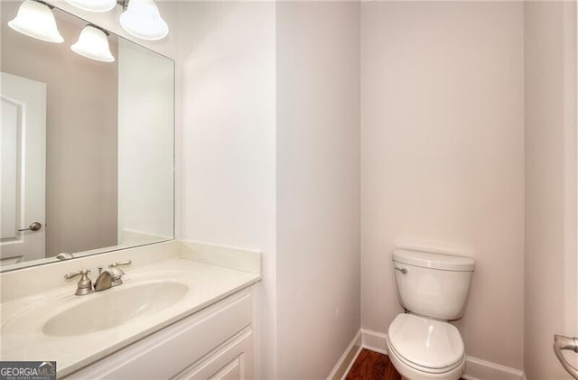 half bathroom with vanity, toilet, and baseboards