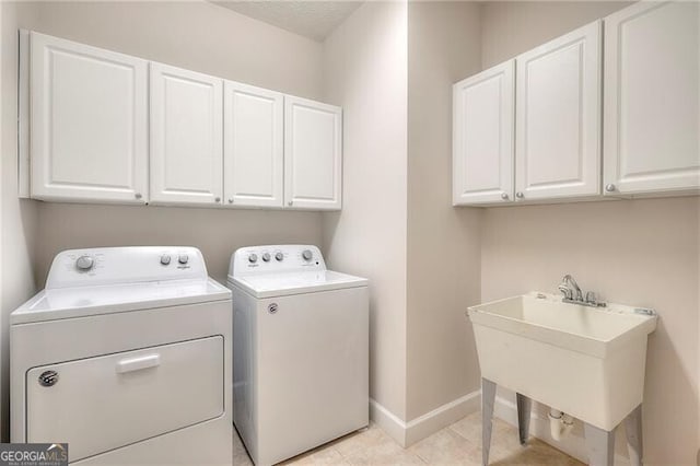 laundry area with light tile patterned floors, cabinet space, washing machine and dryer, a sink, and baseboards