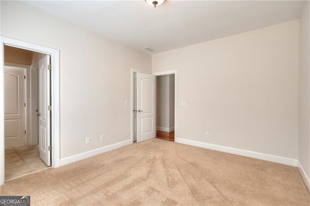 unfurnished bedroom featuring light carpet, visible vents, baseboards, and ensuite bathroom