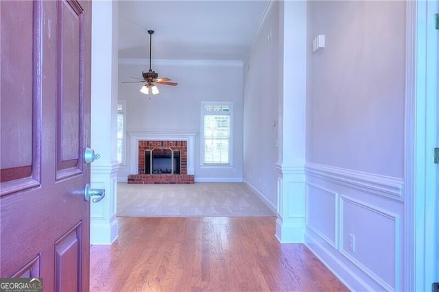 entrance foyer with a decorative wall, ornamental molding, light wood-style floors, a brick fireplace, and ceiling fan