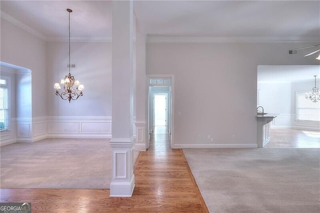 unfurnished dining area featuring a wainscoted wall, a chandelier, crown molding, and wood finished floors