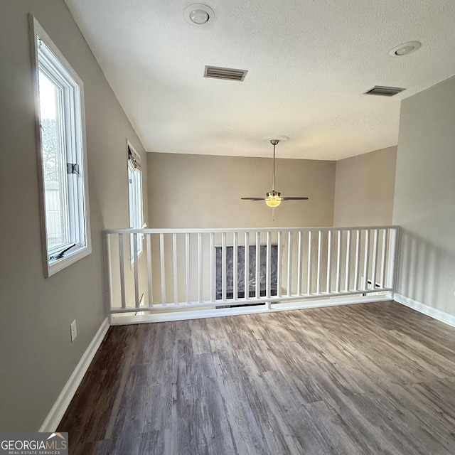 empty room featuring dark wood-style flooring, visible vents, a textured ceiling, and baseboards