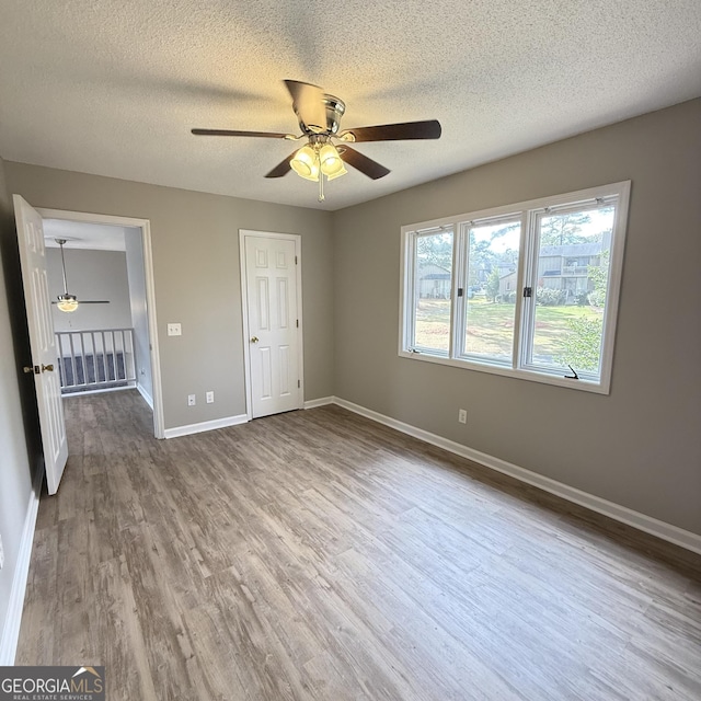 unfurnished bedroom featuring a ceiling fan, a textured ceiling, baseboards, and wood finished floors