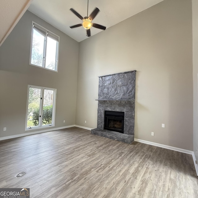 unfurnished living room featuring plenty of natural light, high vaulted ceiling, wood finished floors, and a high end fireplace