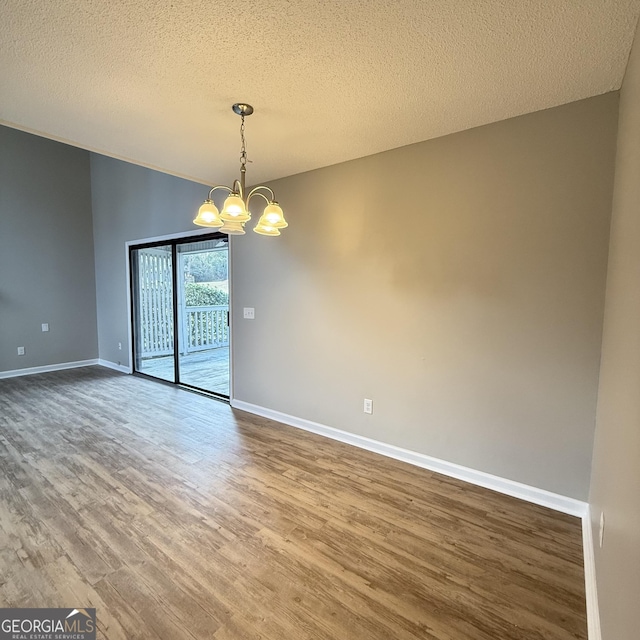 spare room with baseboards, lofted ceiling, wood finished floors, a textured ceiling, and a notable chandelier