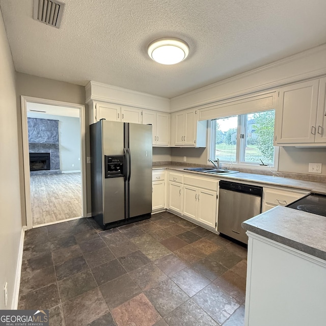 kitchen with a sink, a high end fireplace, visible vents, white cabinets, and appliances with stainless steel finishes