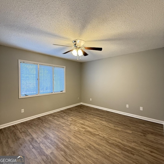 empty room with dark wood-type flooring, a textured ceiling, baseboards, and a ceiling fan