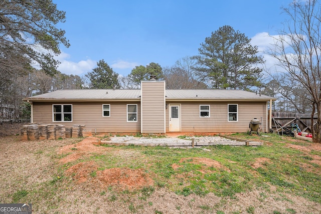 back of property featuring metal roof, a chimney, fence, and a lawn