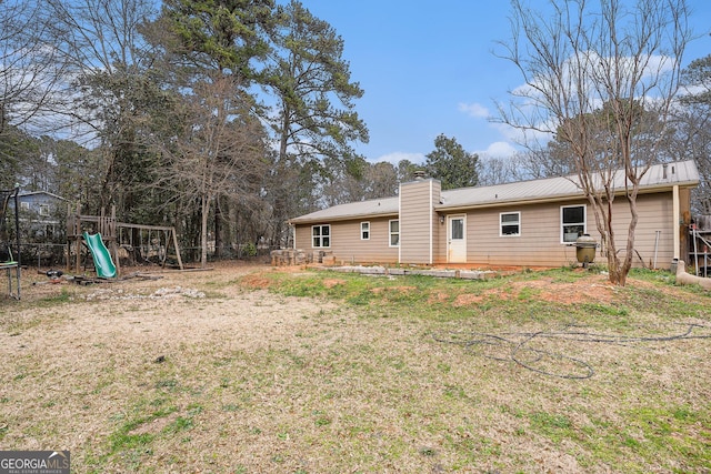 rear view of house featuring metal roof, a playground, a yard, a trampoline, and a chimney