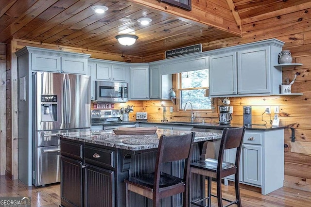 kitchen with dark stone countertops, a kitchen island, appliances with stainless steel finishes, and a sink