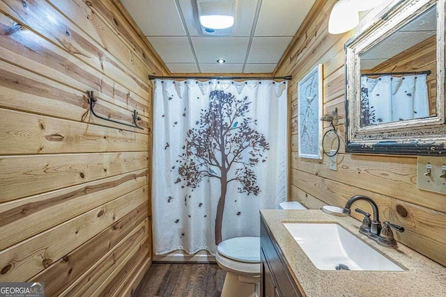 full bathroom with a shower with curtain, wooden walls, toilet, and vanity