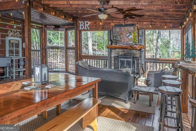 sunroom / solarium with ceiling fan, a wealth of natural light, and a stone fireplace