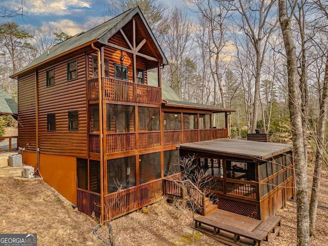 rear view of property featuring central AC unit, log veneer siding, and a sunroom