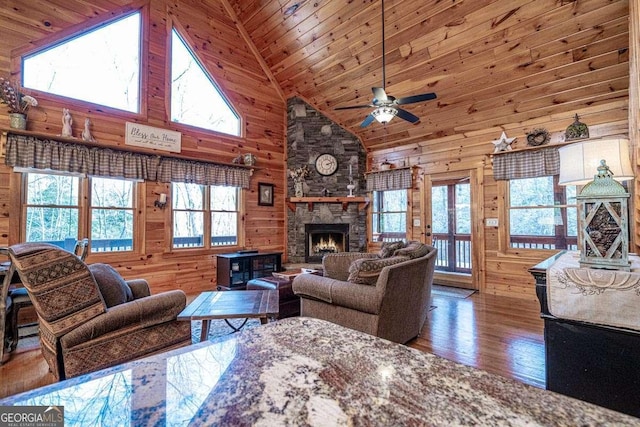 living area featuring wooden ceiling, wood walls, a stone fireplace, and wood finished floors