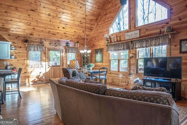 living area with high vaulted ceiling, a notable chandelier, wood walls, and wood finished floors