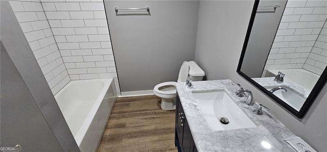 bathroom featuring toilet, tub / shower combination, vanity, wood finished floors, and baseboards