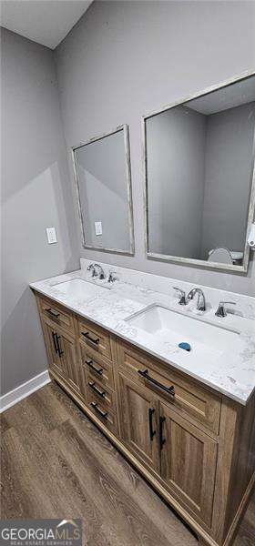 full bath featuring double vanity, a sink, baseboards, and wood finished floors