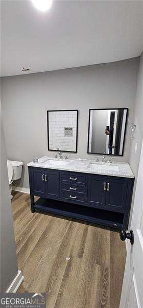 full bathroom with double vanity, a sink, toilet, and wood finished floors